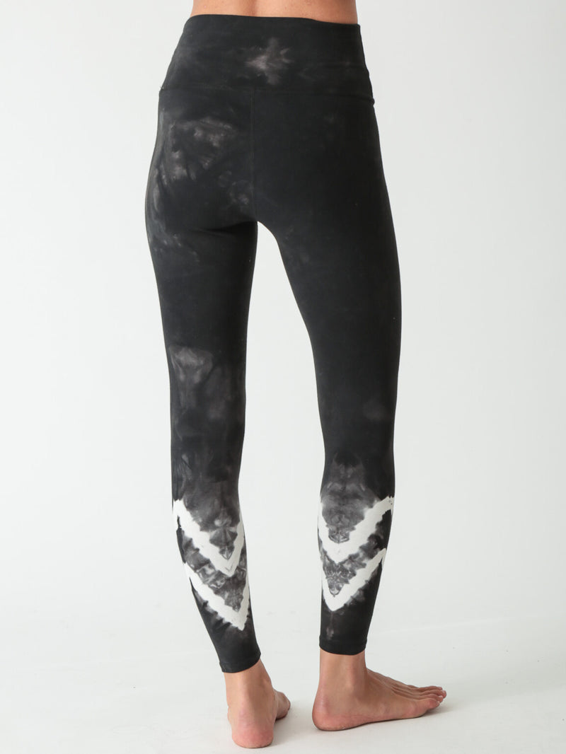 Mineral-washed black high-waisted leggings featuring white tie-dye chevron patterns at the lower legs.