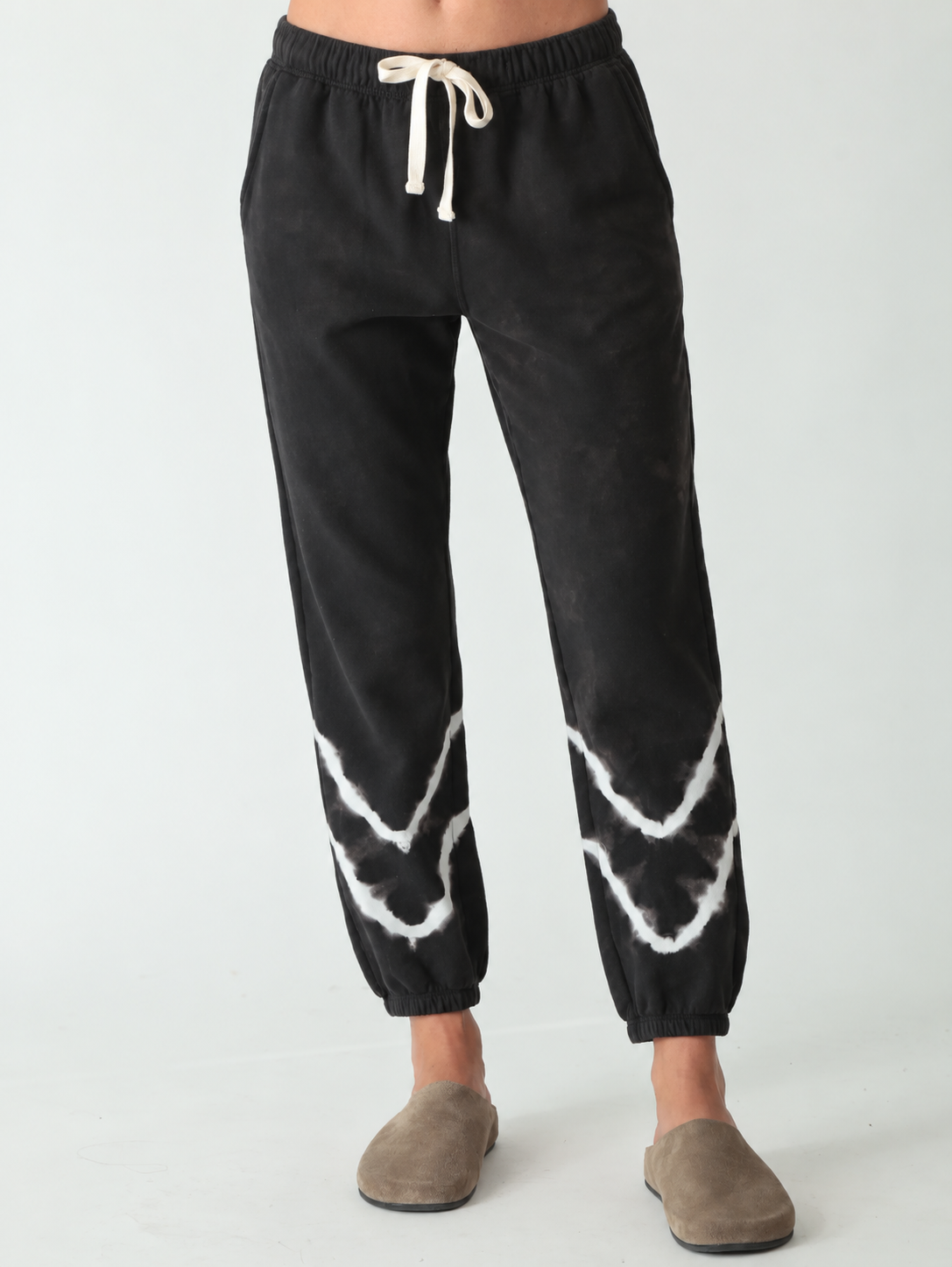 Woman wearing black jogger sweatpants with white wave detail and taupe suede clogs