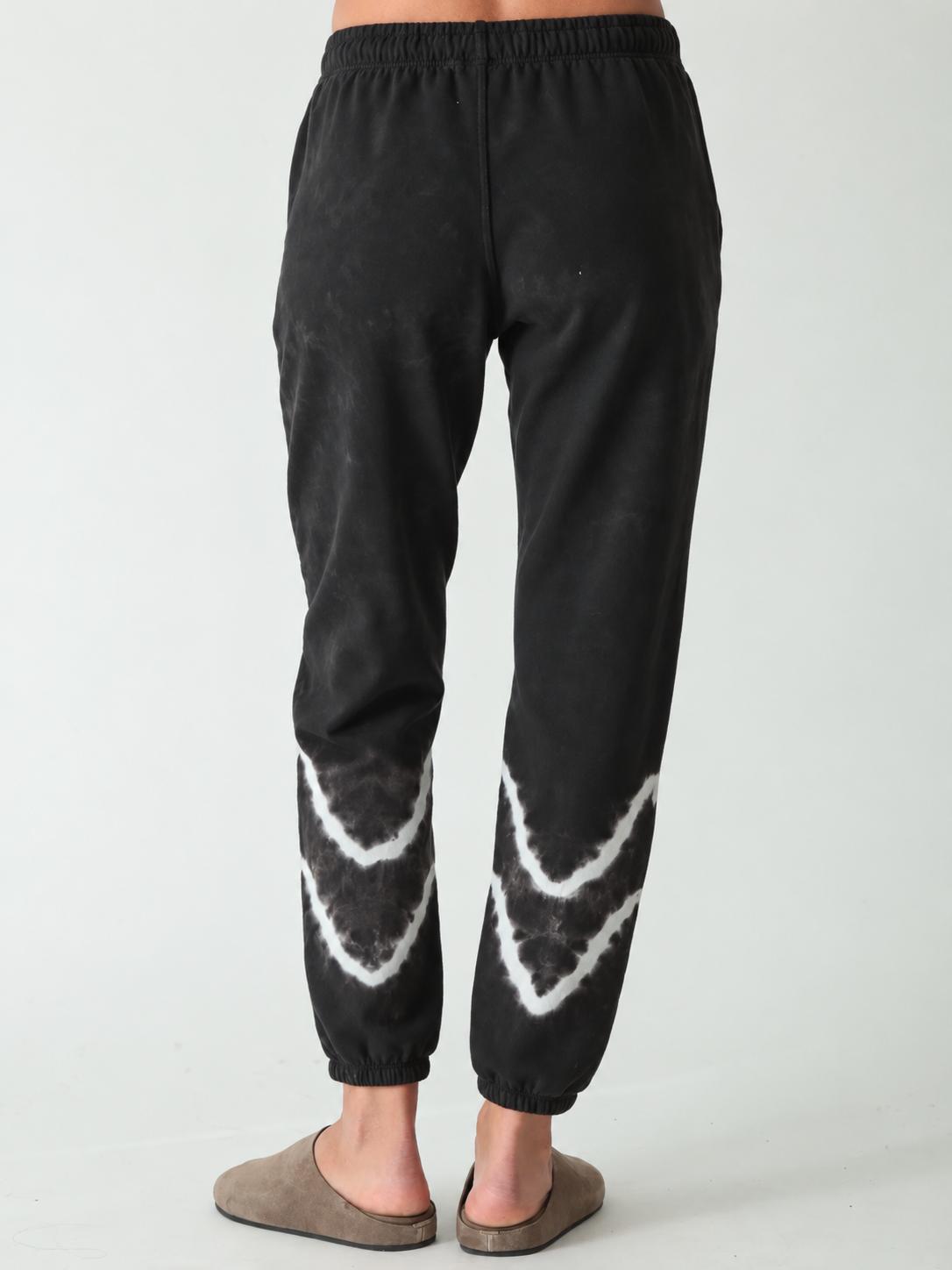 Woman wearing black jogger sweatpants with white wave detail and taupe suede clogs