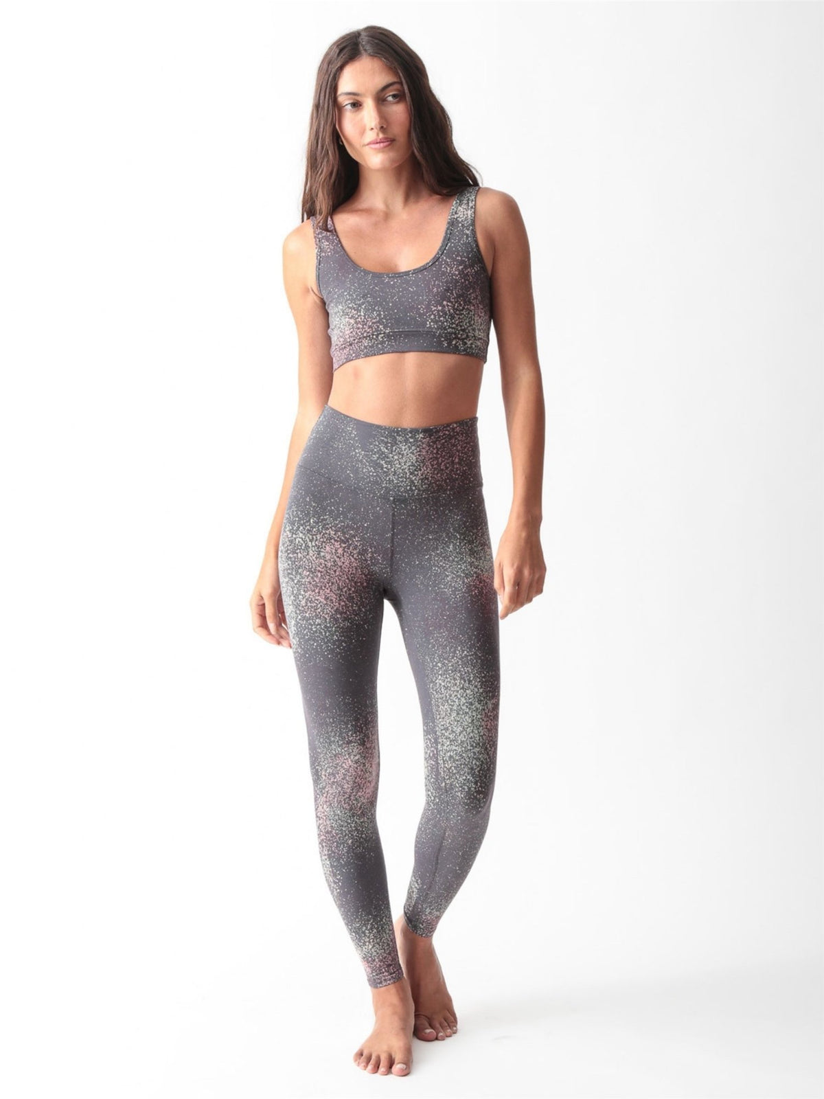 Woman wearing a charcoal gray scoop-neck sports bra and matching high-waisted leggings with a pink and sage speckled print by Electric & Rose