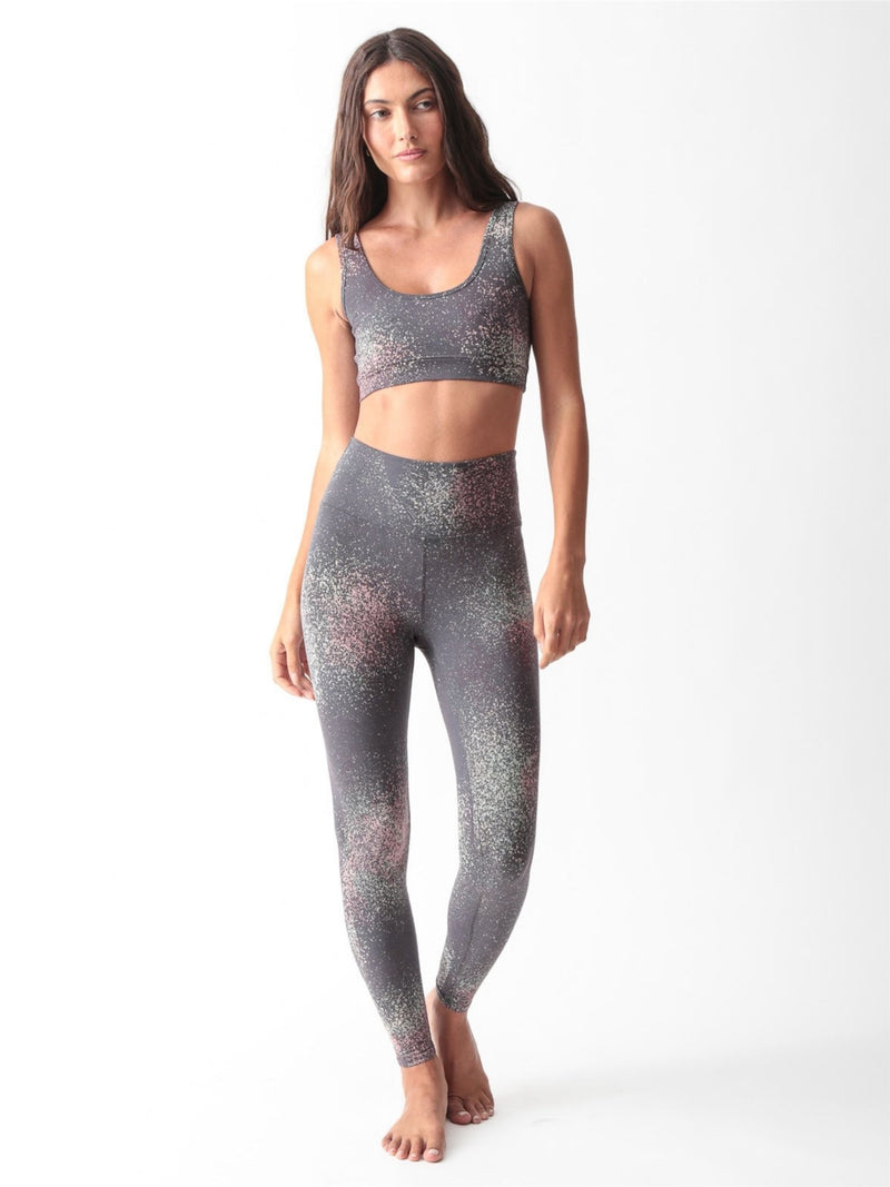 Woman wearing a charcoal gray scoop-neck sports bra and matching high-waisted leggings with a pink and sage speckled print by Electric & Rose