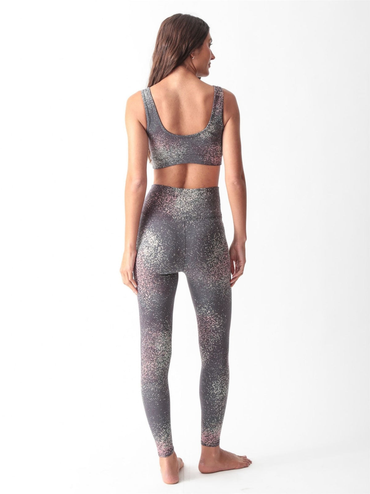 Woman wearing a charcoal gray scoop-neck sports bra and matching high-waisted leggings with a pink and sage speckled print by Electric & Rose