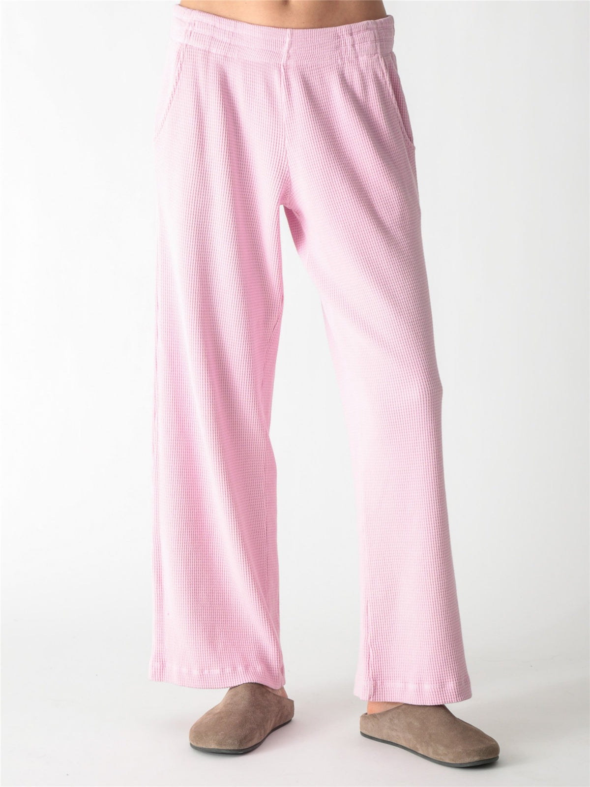 A woman wearing a light pink, long-sleeve waffle-knit lounge set with wide-leg pants against a plain white background.