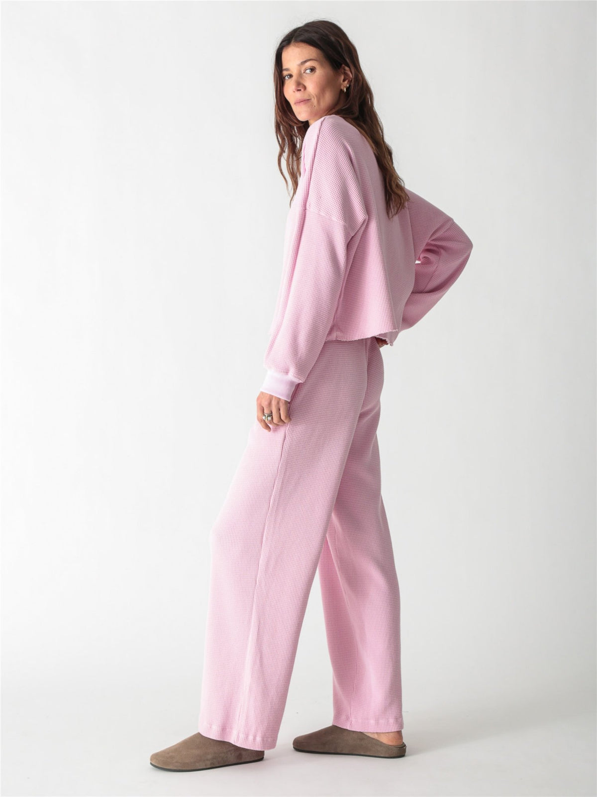 A woman wearing a light pink, long-sleeve waffle-knit lounge set with wide-leg pants against a plain white background.