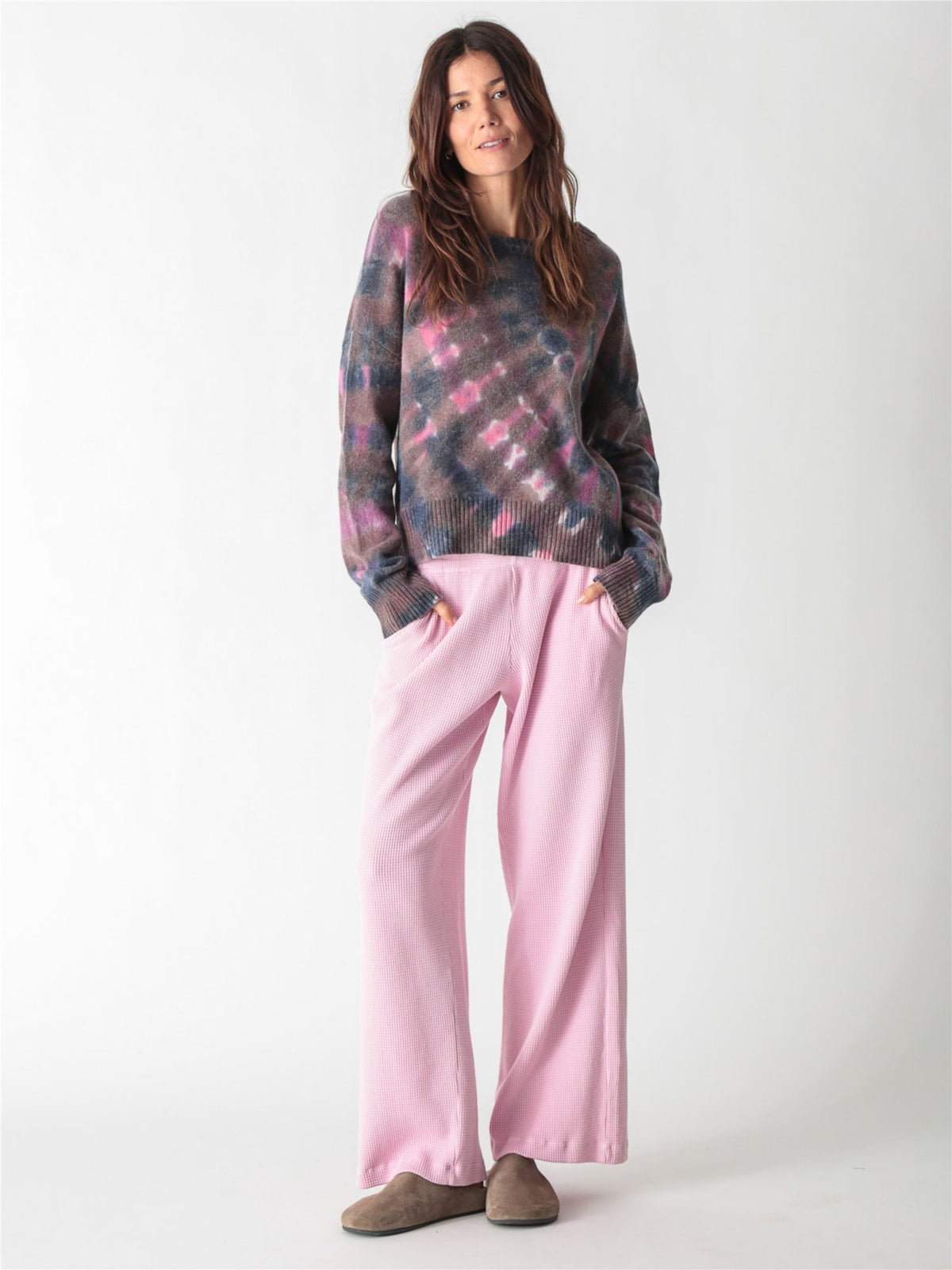 A woman wearing a light pink, long-sleeve waffle-knit lounge set with wide-leg pants against a plain white background.