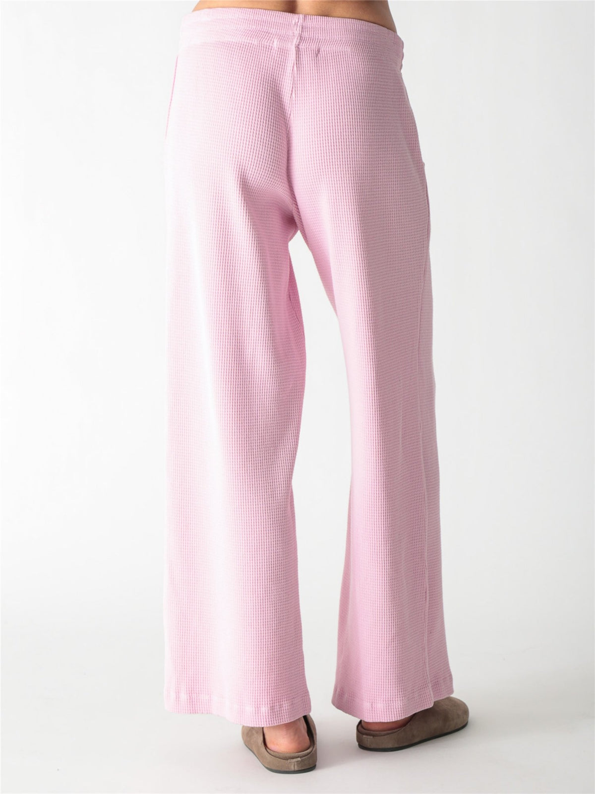 A woman wearing a light pink, long-sleeve waffle-knit lounge set with wide-leg pants against a plain white background.