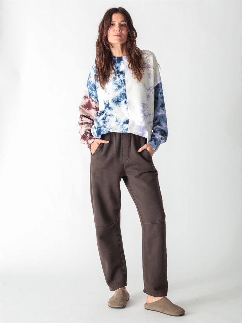 A person wearing dark brown relaxed-fit fleece sweatpants with elastic waistband, side pockets, and knee seams, paired with tan suede slip-on shoes against a plain white background.