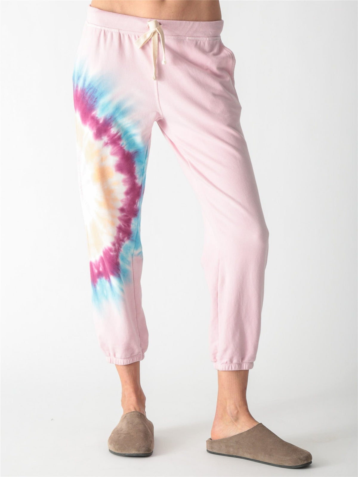 Light pink sweatpants featuring a drawstring waist, side pockets, elastic cuffs, and a vibrant tie-dye accent panel along the right leg.