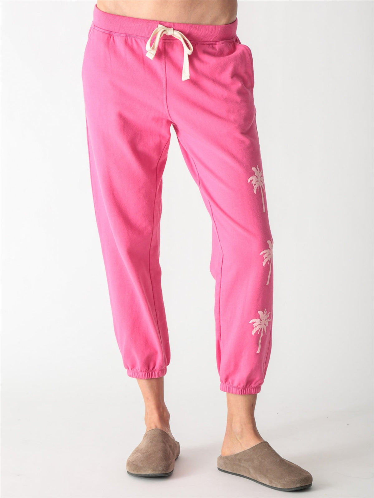 Bright pink jogger sweatpants with an off-white drawstring waist and small pale pink palm tree graphics printed down the left leg.