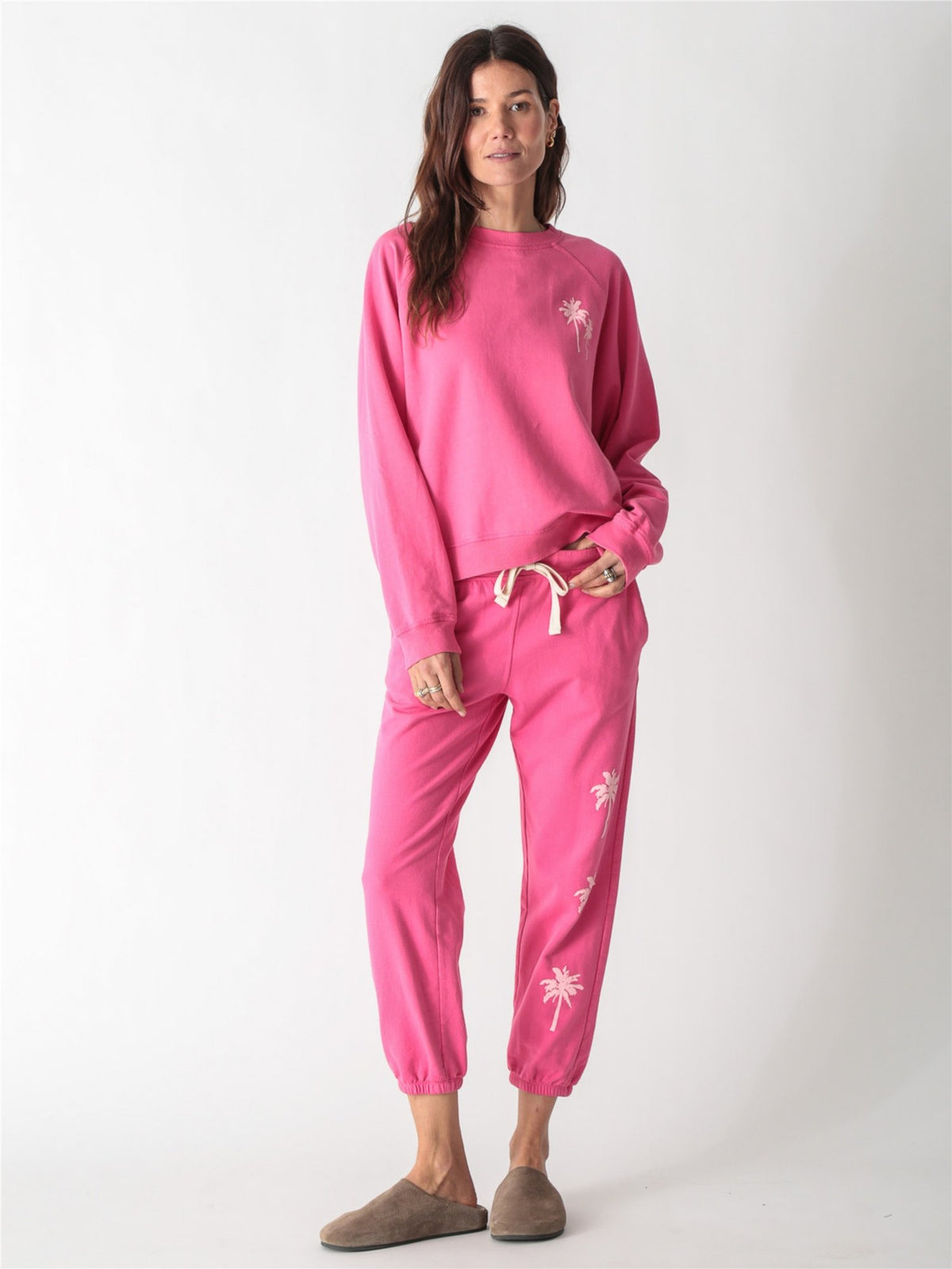 Bright pink jogger sweatpants with an off-white drawstring waist and small pale pink palm tree graphics printed down the left leg.