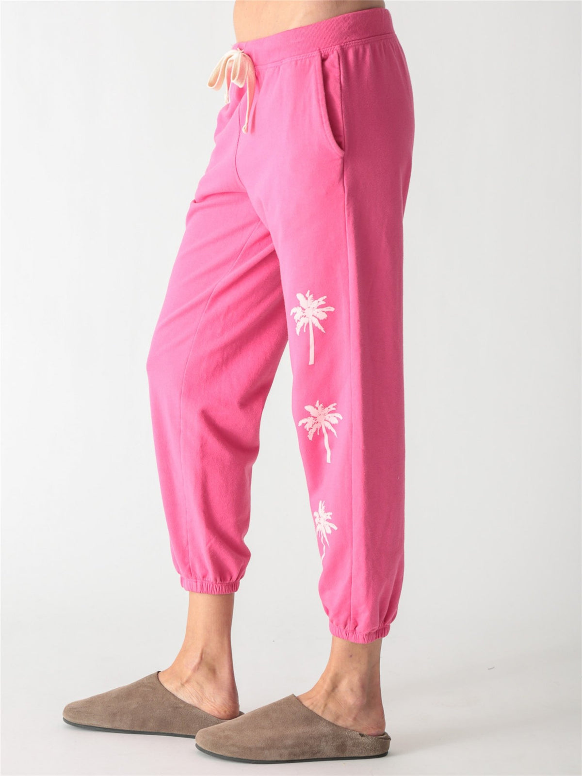 Bright pink jogger sweatpants with an off-white drawstring waist and small pale pink palm tree graphics printed down the left leg.