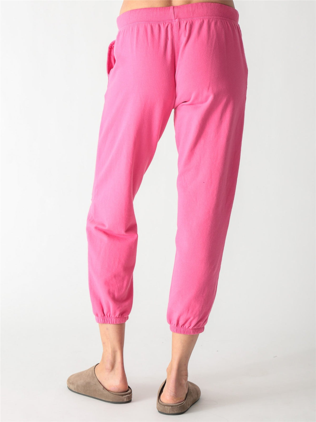 Bright pink jogger sweatpants with an off-white drawstring waist and small pale pink palm tree graphics printed down the left leg.