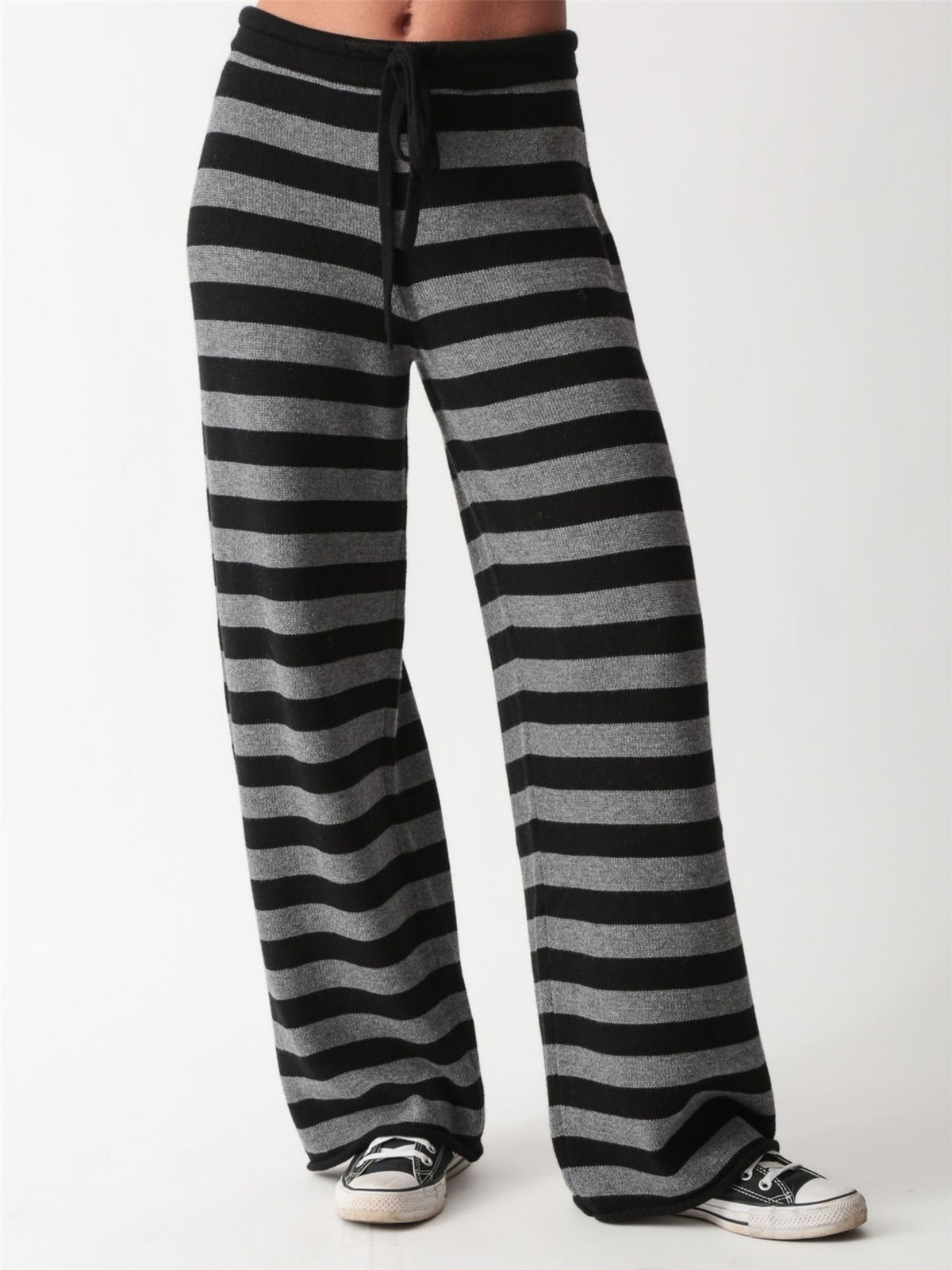 Woman wearing a black and heather grey striped knit crewneck sweater with matching wide-leg drawstring knit pants and white sneakers.