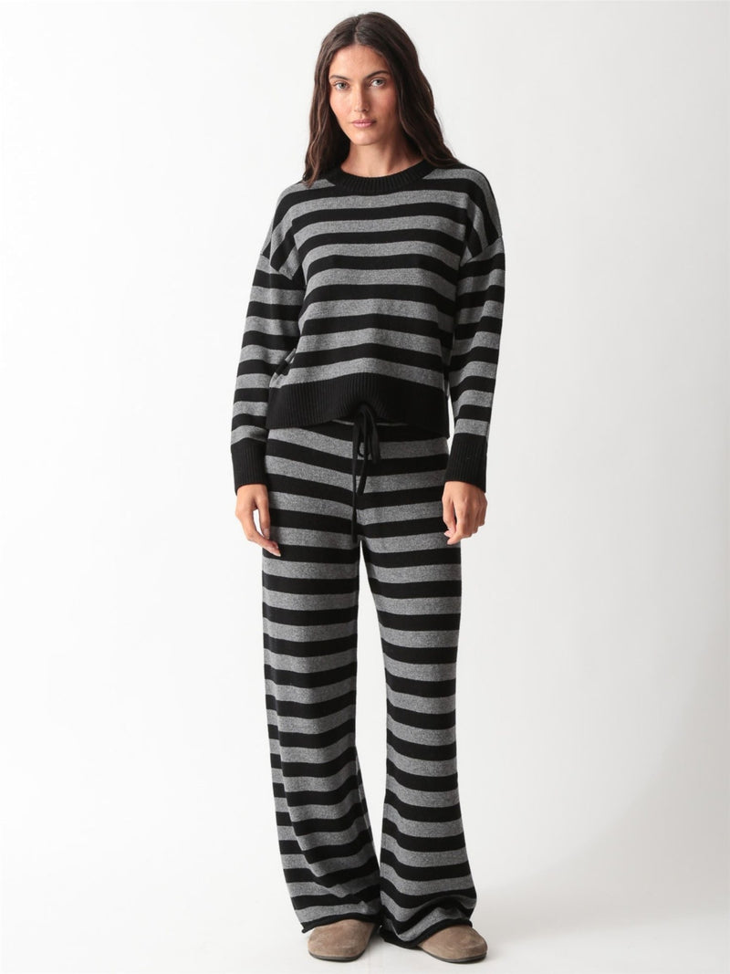Woman wearing a black and heather grey striped knit crewneck sweater with matching wide-leg drawstring knit pants and slides.