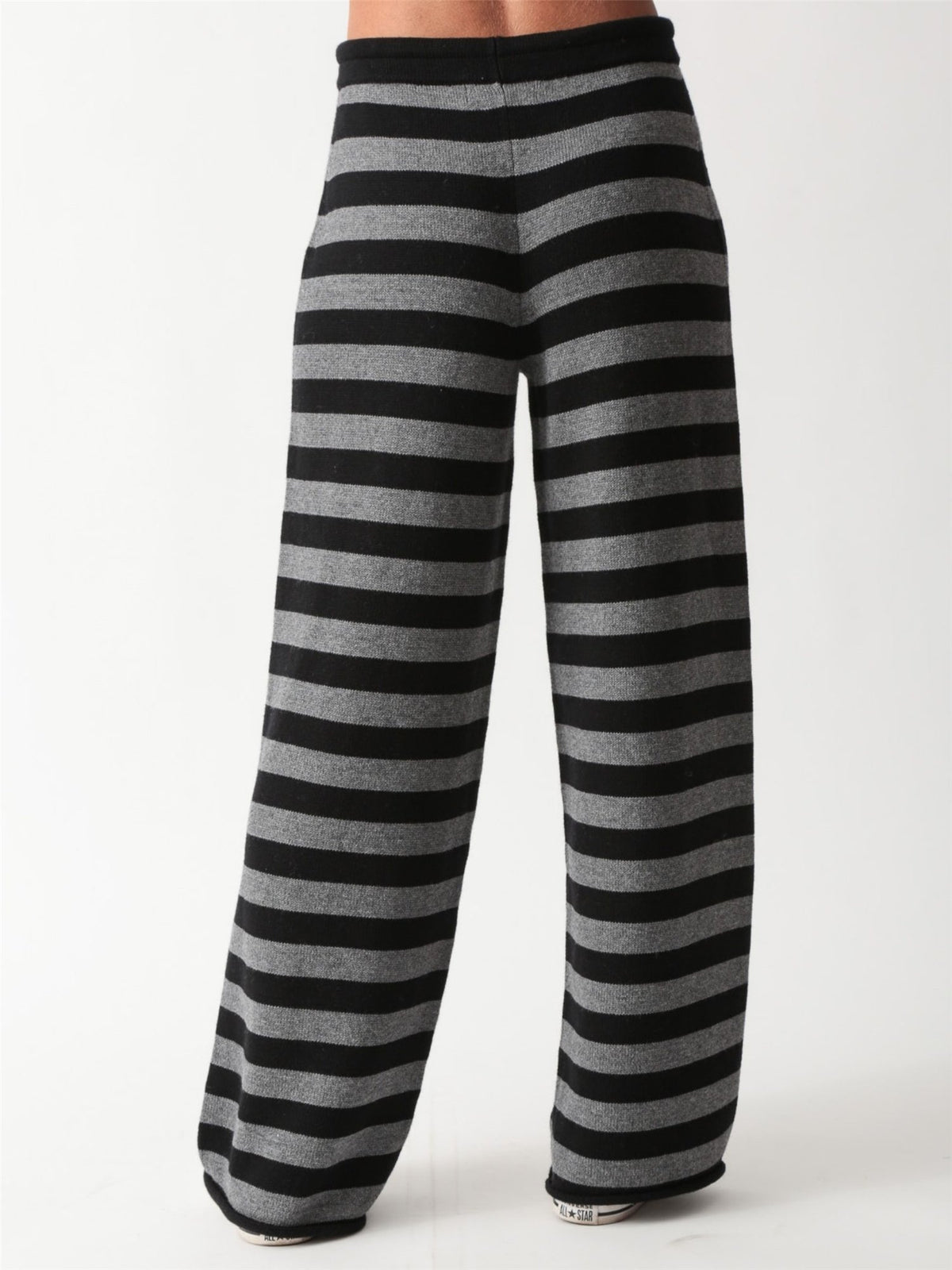 Woman wearing a black and heather grey striped knit crewneck sweater with matching wide-leg drawstring knit pants and white sneakers.