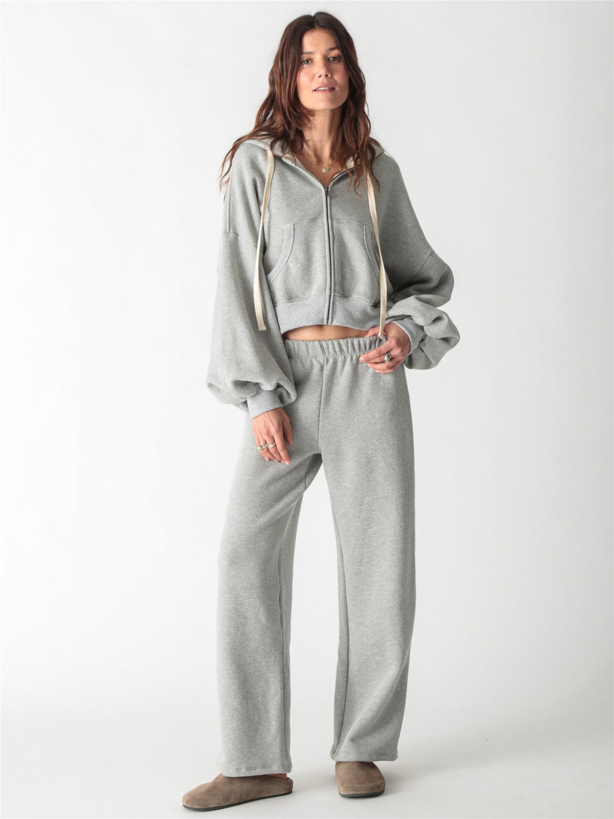 A woman wearing a heather gray cropped zip-up hoodie with voluminous sleeves and matching wide-leg sweatpants against a white background.