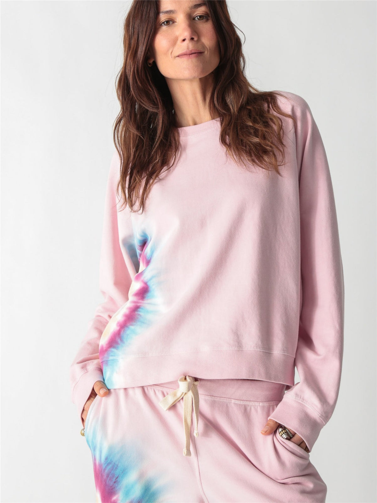 A light pink crewneck sweatshirt with long sleeves, ribbed trim, and a colorful tie-dye stripe down the right side.