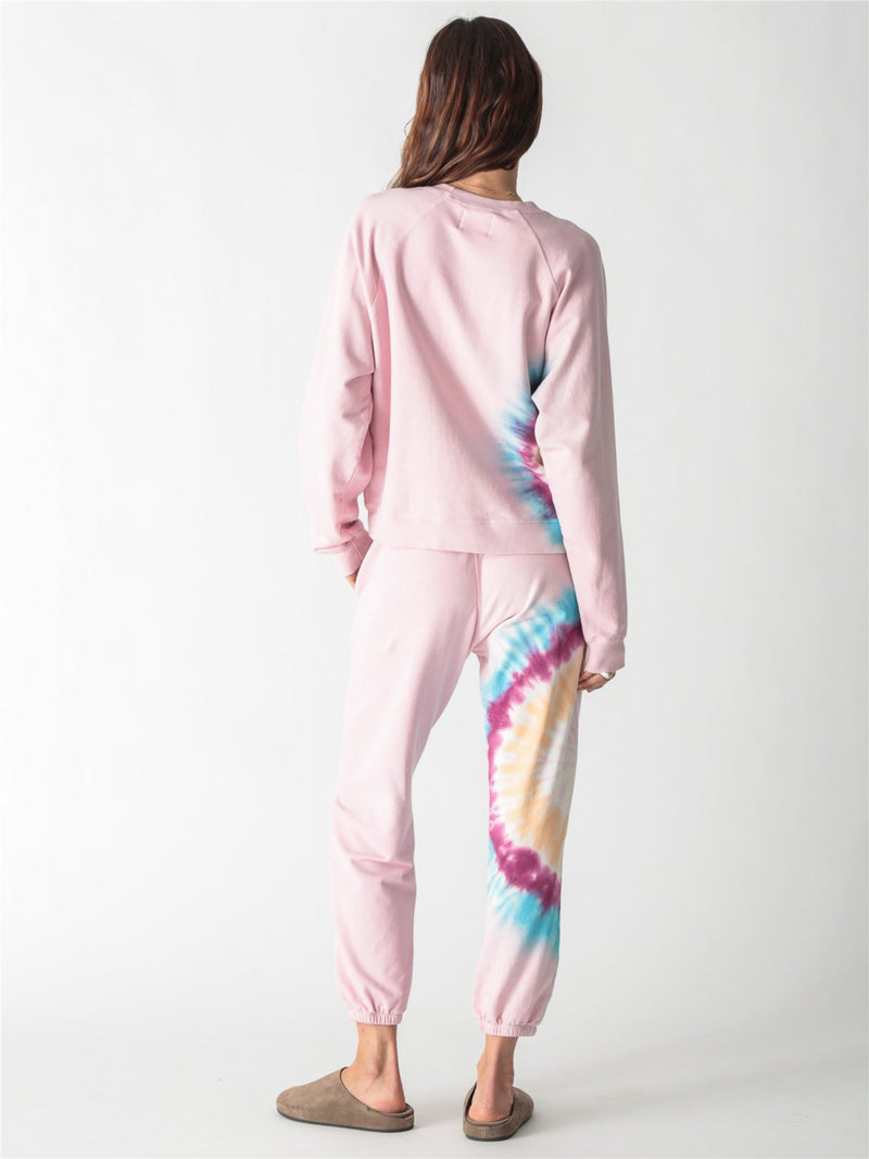 A light pink crewneck sweatshirt with long sleeves, ribbed trim, and a colorful tie-dye stripe down the right side.
