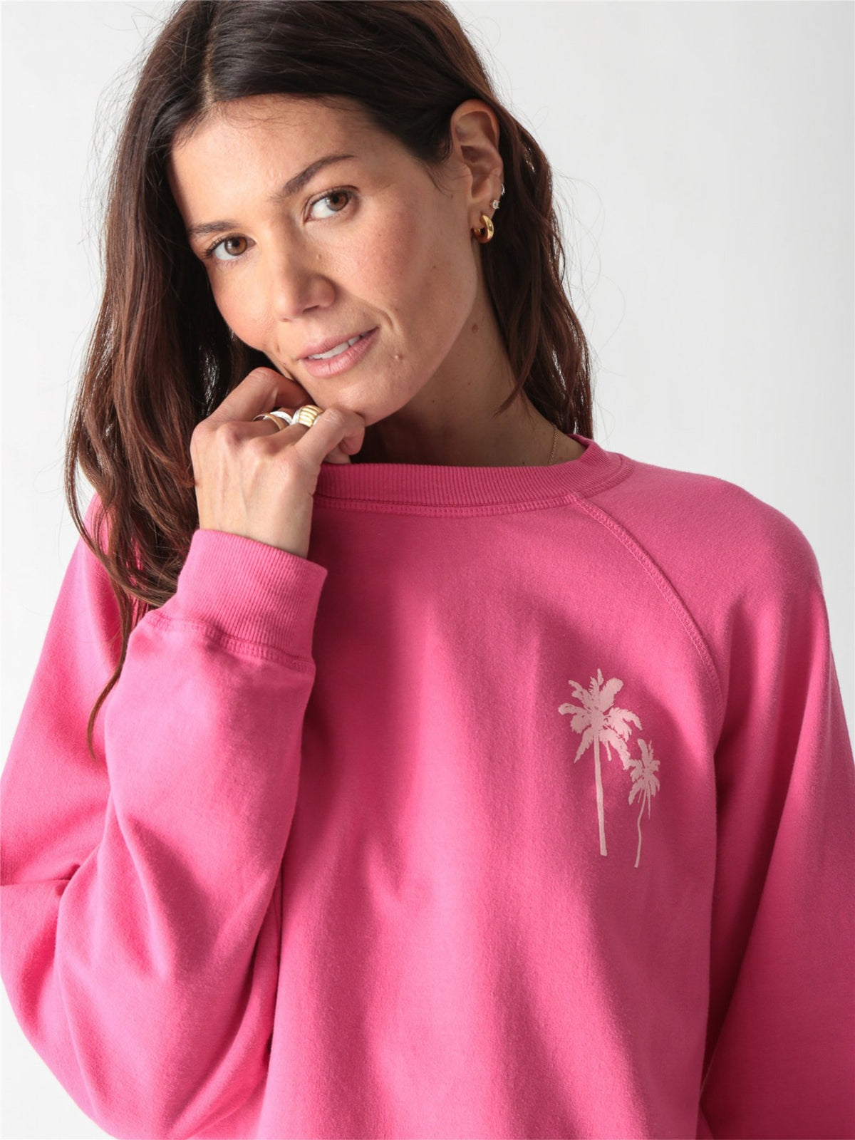 Bright pink crewneck sweatshirt featuring a small pale pink palm tree graphic on the left chest.