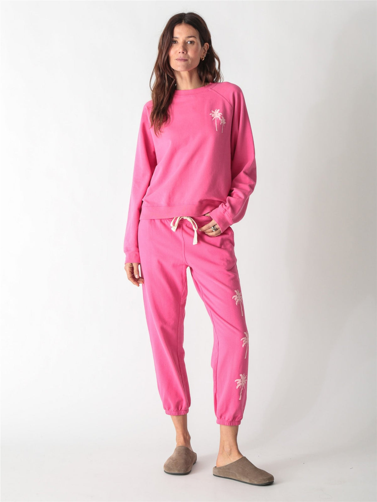 Bright pink crewneck sweatshirt featuring a small pale pink palm tree graphic on the left chest.