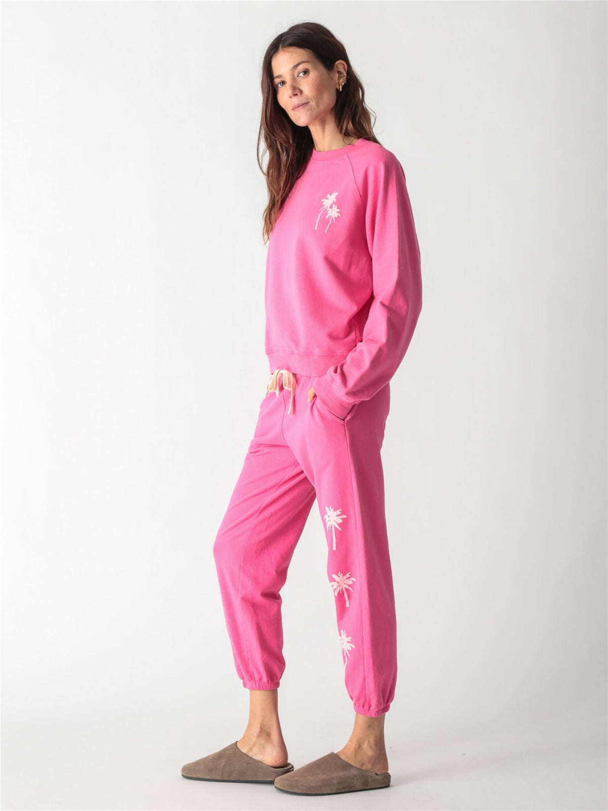 Bright pink crewneck sweatshirt featuring a small pale pink palm tree graphic on the left chest.