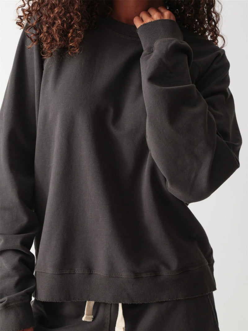 Woman wearing a washed charcoal raglan crewneck sweatshirt with matching drawstring jogger sweatpants and suede clogs.