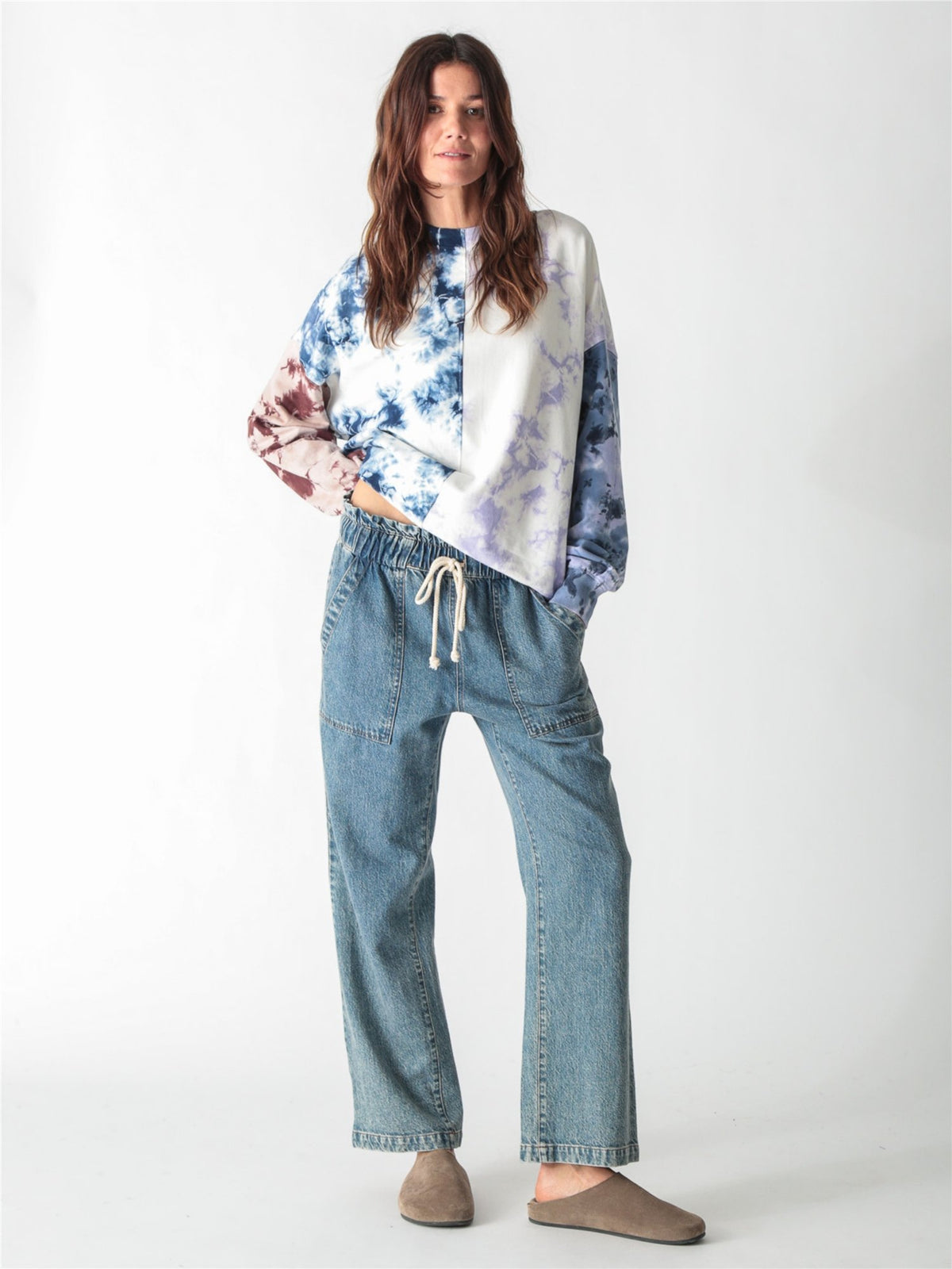 A woman wearing an oversized, multi-color tie-dye sweatshirt featuring split panels of blue, purple, and brown tie-dye patterns set against a white background.