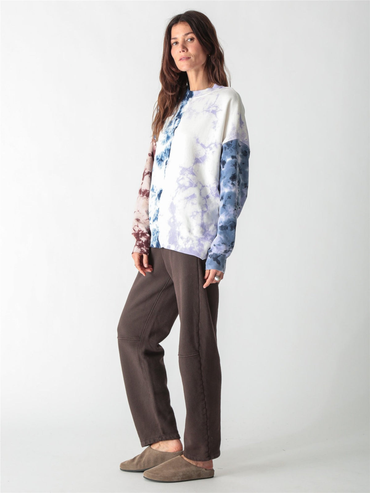 A woman wearing an oversized, multi-color tie-dye sweatshirt featuring split panels of blue, purple, and brown tie-dye patterns set against a white background.