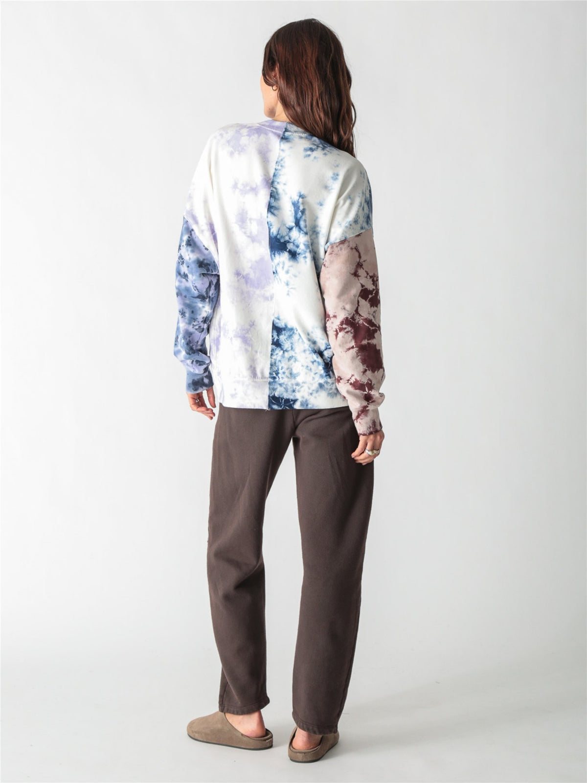 A woman wearing an oversized, multi-color tie-dye sweatshirt featuring split panels of blue, purple, and brown tie-dye patterns set against a white background.