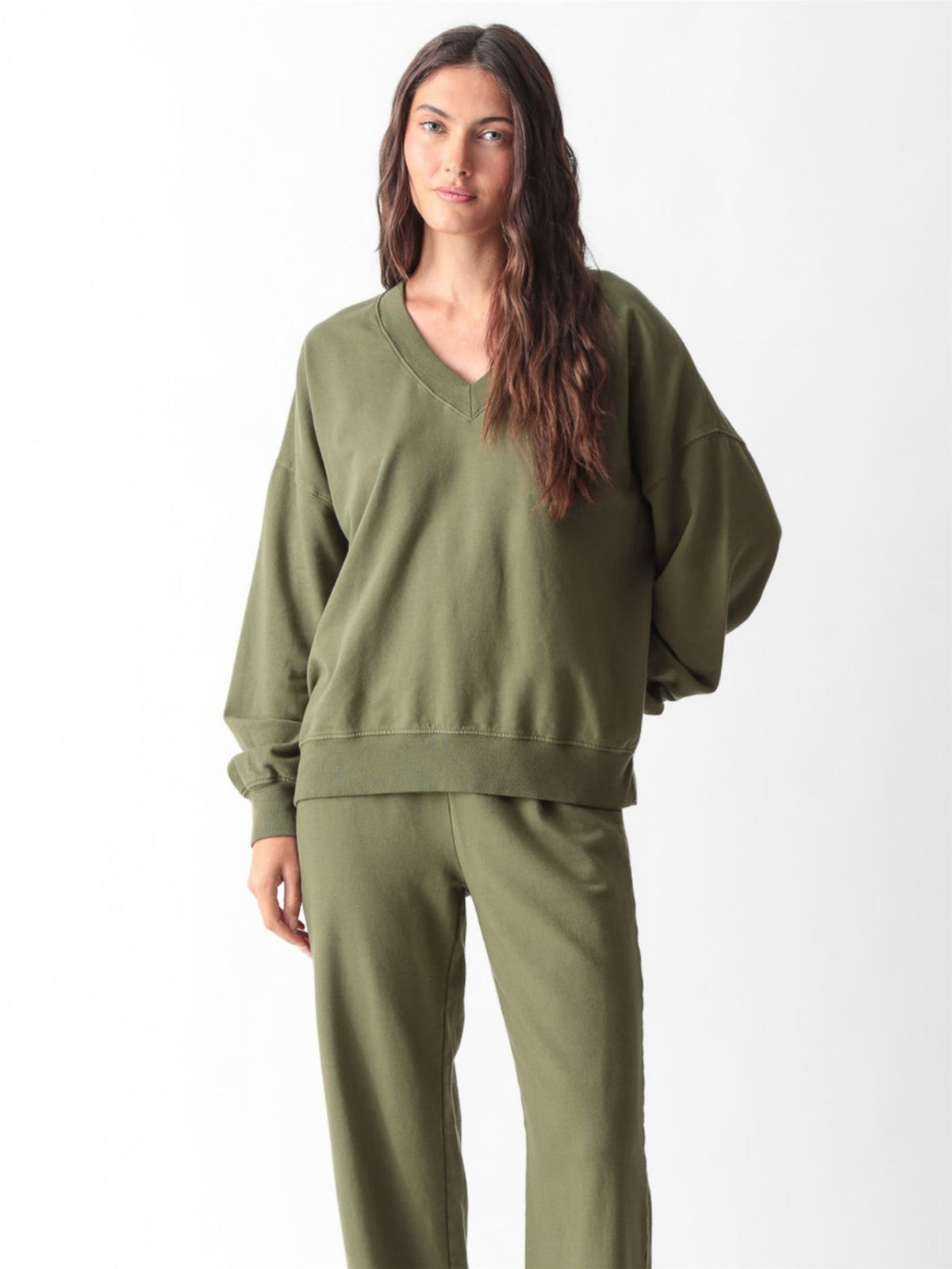 Woman wearing an olive green oversized V-neck sweatshirt with balloon sleeves and matching wide-leg sweatpants by Electric & Rose