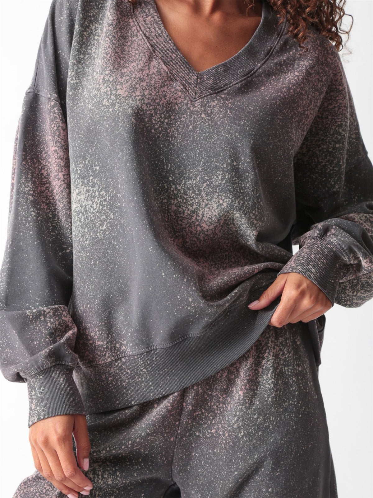 Woman wearing a charcoal gray oversized V-neck French terry sweatshirt with a pink and sage speckled dye print and matching wide-leg sweatpants by Electric & Rose