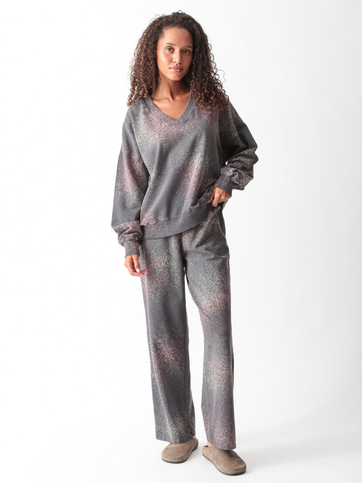 Woman wearing a charcoal gray oversized V-neck French terry sweatshirt with a pink and sage speckled dye print and matching wide-leg sweatpants by Electric & Rose