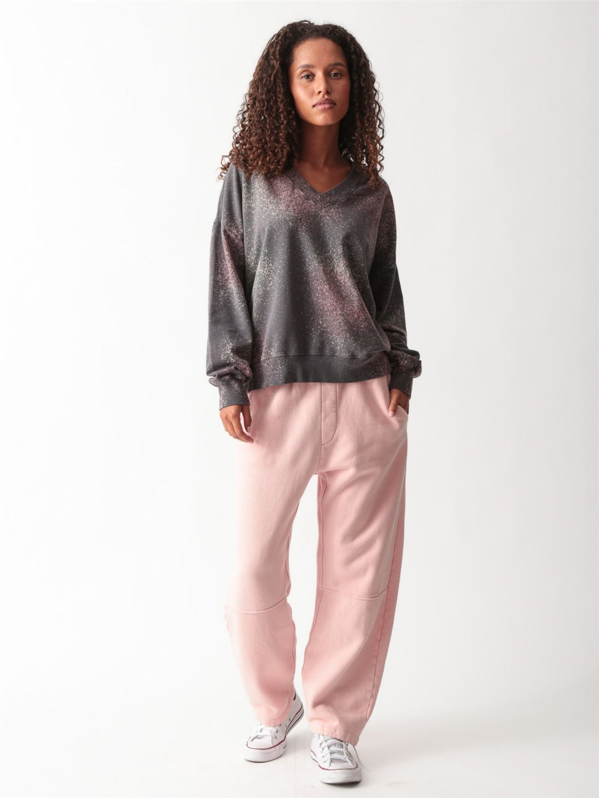 Woman wearing a charcoal gray oversized V-neck French terry sweatshirt with a pink and sage speckled dye print and matching wide-leg sweatpants by Electric & Rose