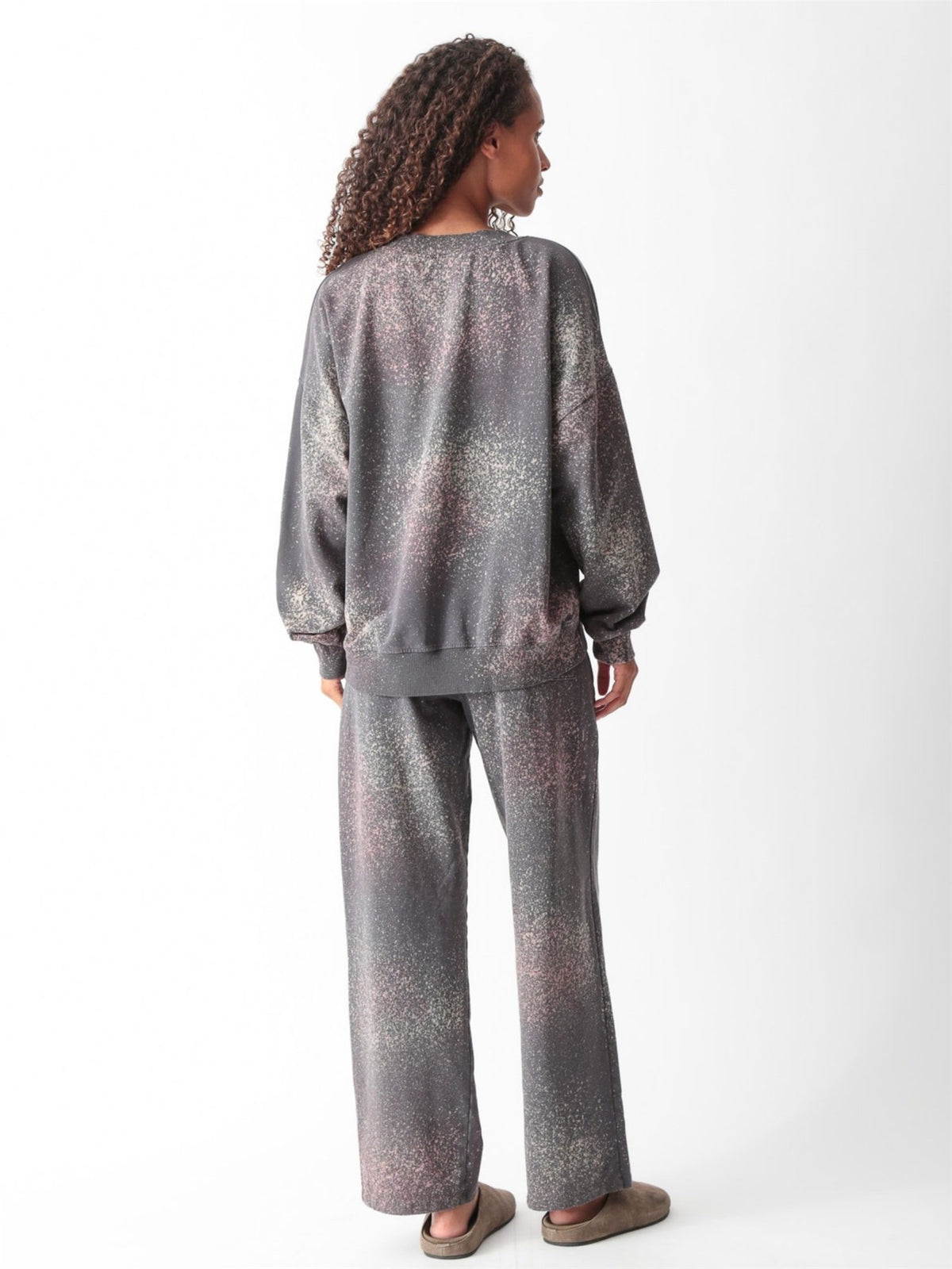 Woman wearing a charcoal gray oversized V-neck French terry sweatshirt with a pink and sage speckled dye print and matching wide-leg sweatpants by Electric & Rose
