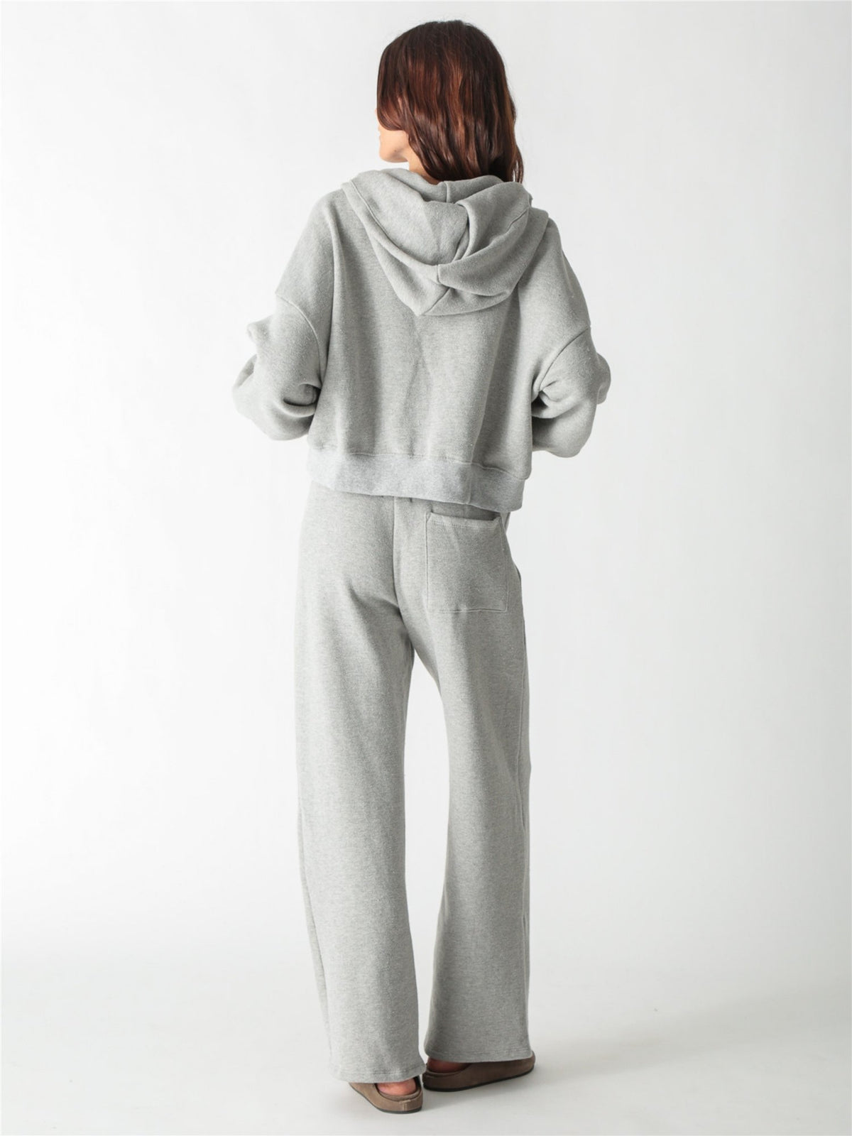 A woman wearing a heather gray cropped zip-up hoodie with voluminous sleeves and matching wide-leg sweatpants against a white background.