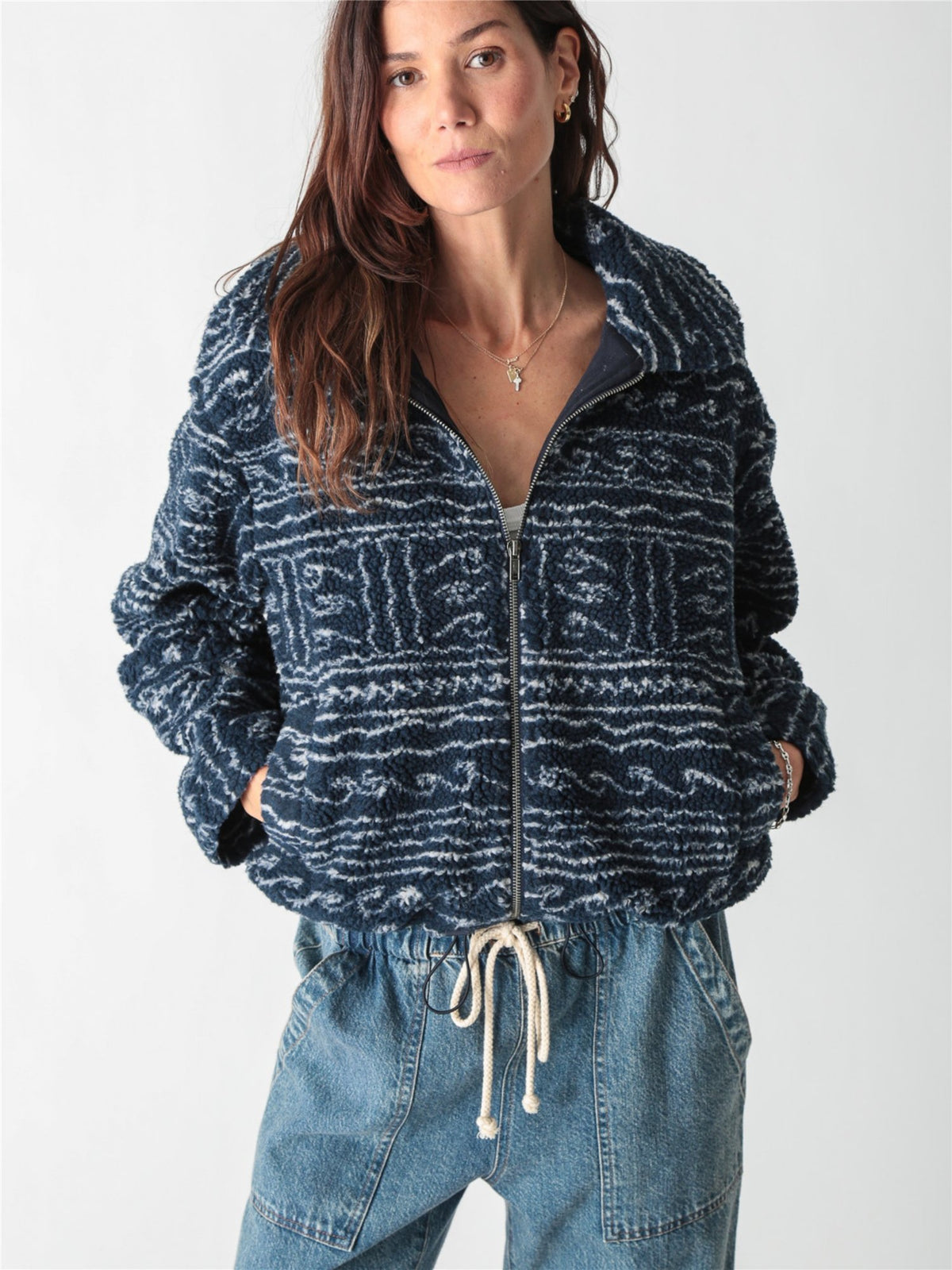 A woman wearing a dark blue and white patterned fleece zip-up jacket paired with drawstring denim jeans against a plain white background.