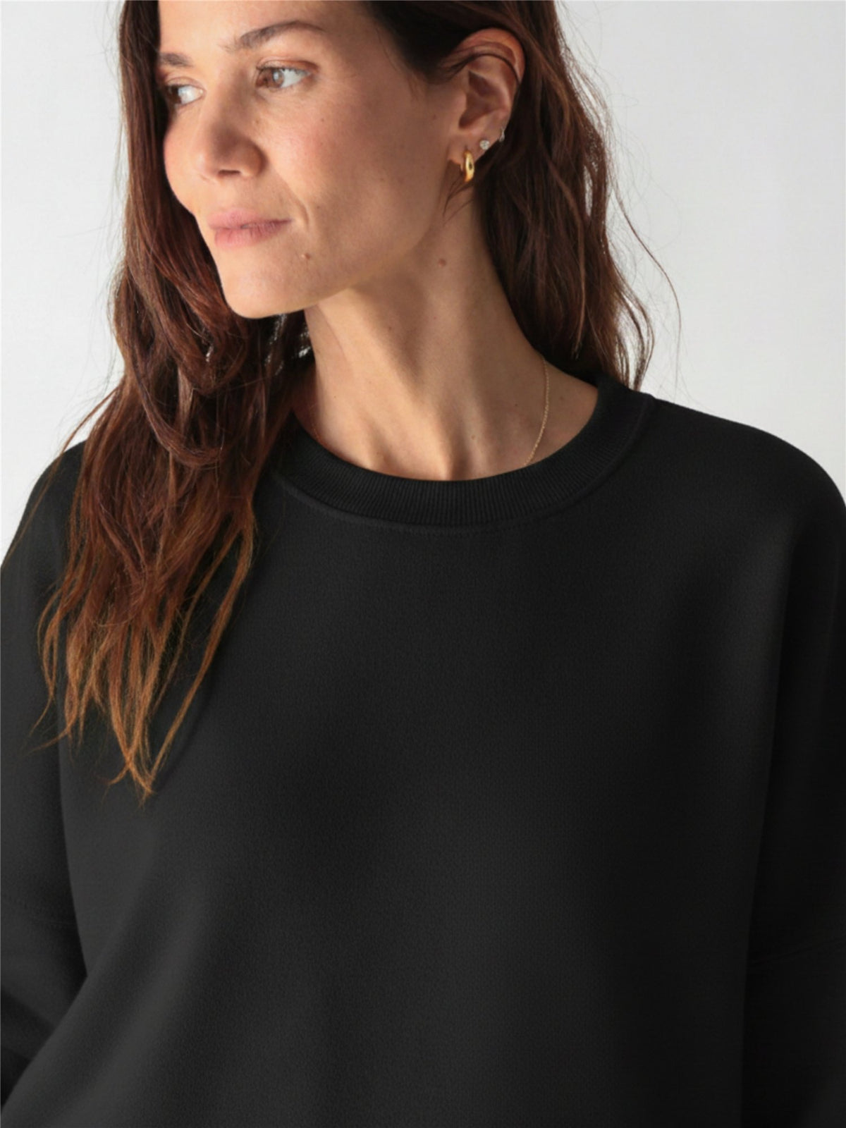 A woman wearing a black crewneck sweatshirt with ribbed cuffs and matching sweatpants against a white background.