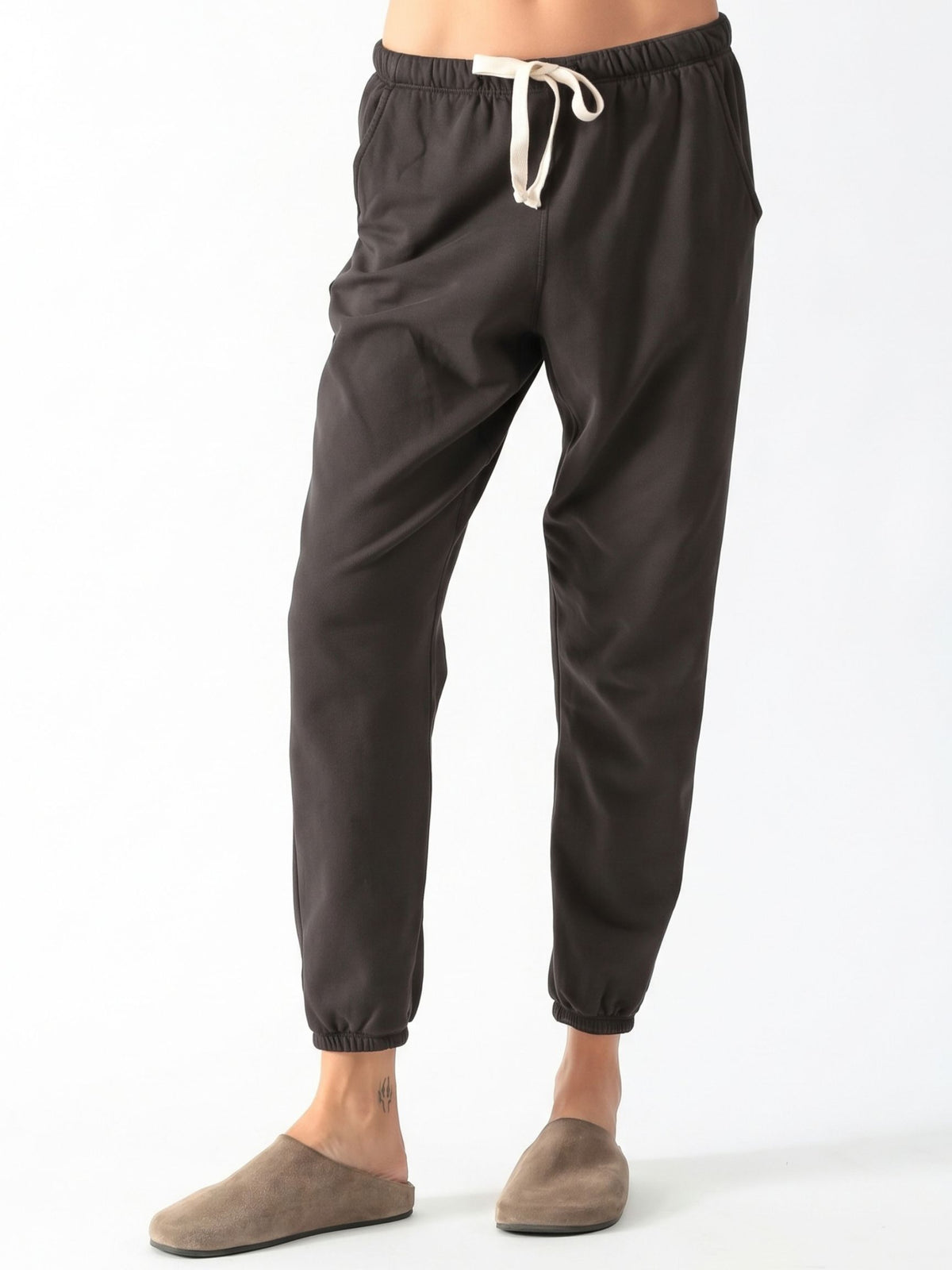Woman wearing a washed charcoal raglan crewneck sweatshirt with matching drawstring jogger sweatpants and suede clogs.
