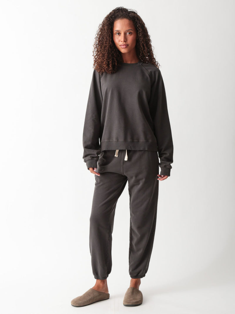 Woman wearing a washed charcoal raglan crewneck sweatshirt with matching drawstring jogger sweatpants and suede clogs.