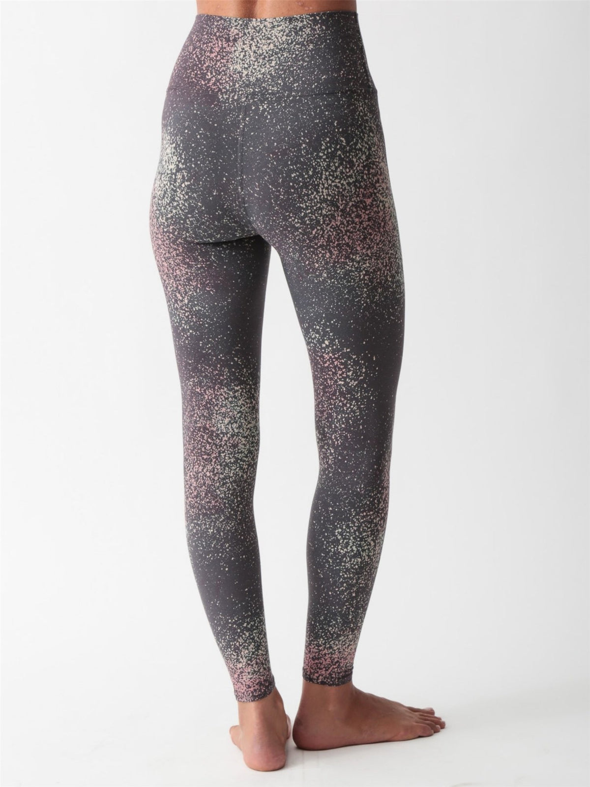 Woman wearing a charcoal gray scoop-neck sports bra and matching high-waisted leggings with a pink and sage speckled print by Electric & Rose