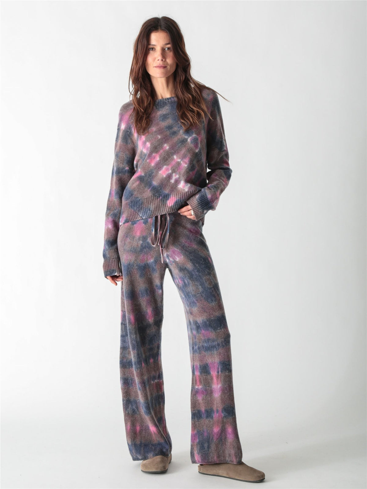 A long-sleeve, relaxed-fit knit sweater with a moody tie-dye pattern in shades of charcoal gray, muted purple, and bright pink accents.
