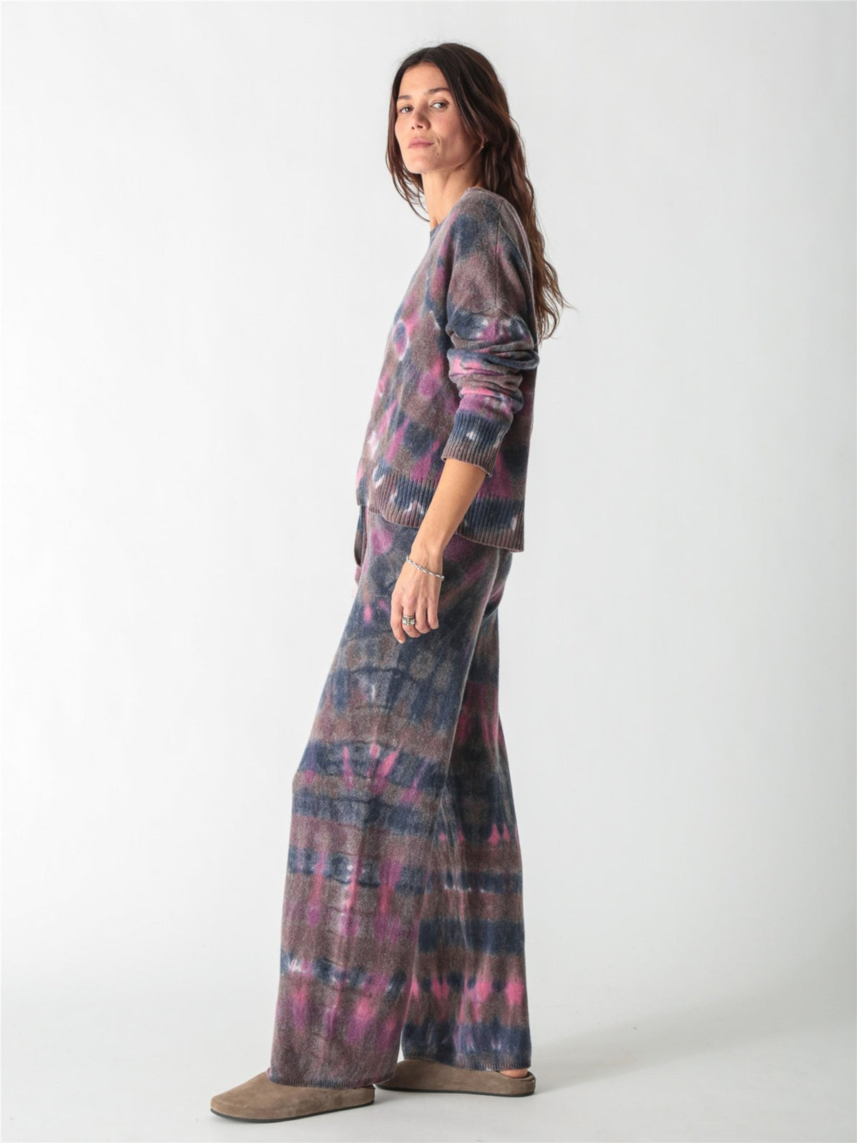 A long-sleeve, relaxed-fit knit sweater with a moody tie-dye pattern in shades of charcoal gray, muted purple, and bright pink accents.