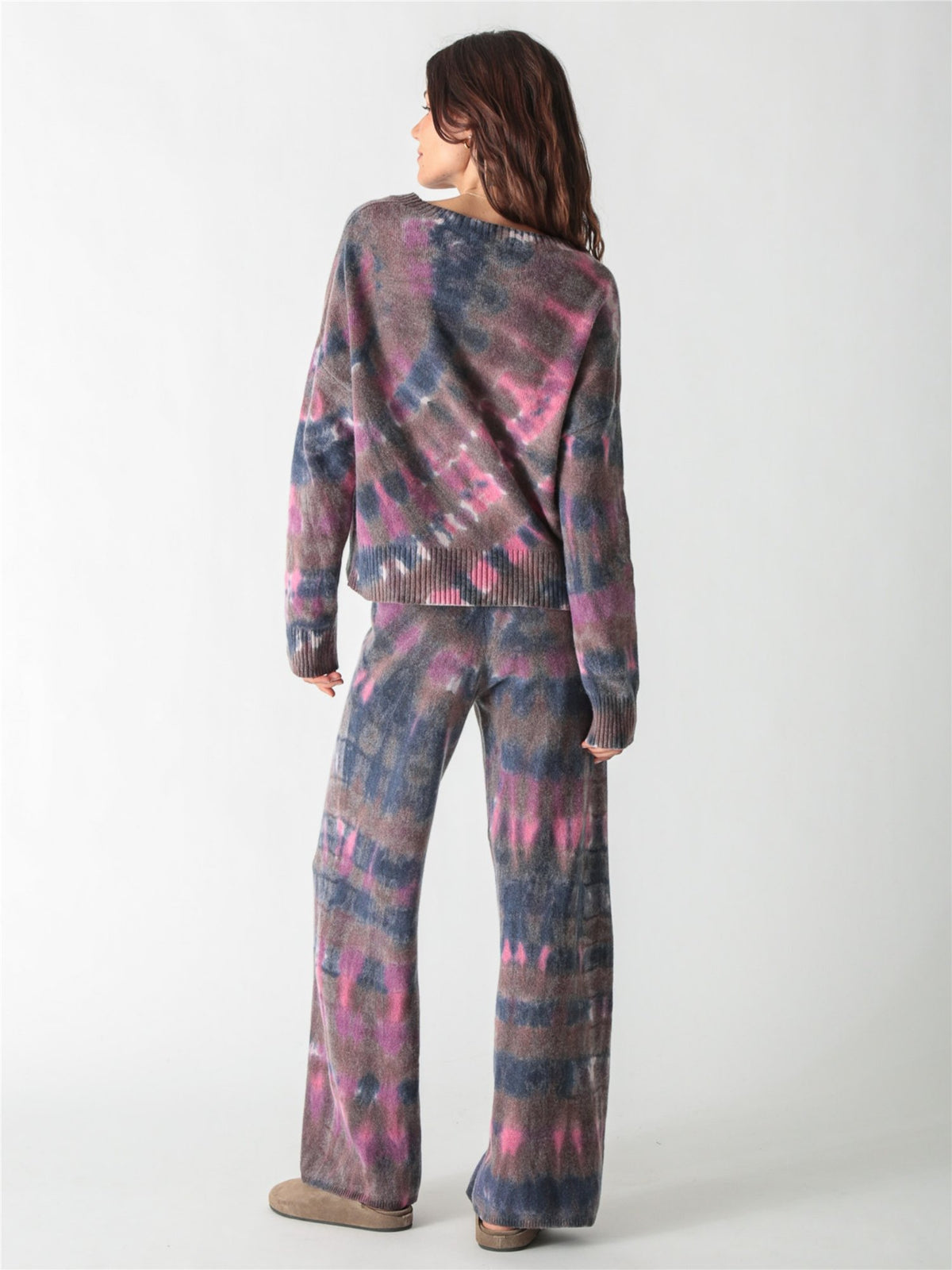 A long-sleeve, relaxed-fit knit sweater with a moody tie-dye pattern in shades of charcoal gray, muted purple, and bright pink accents.