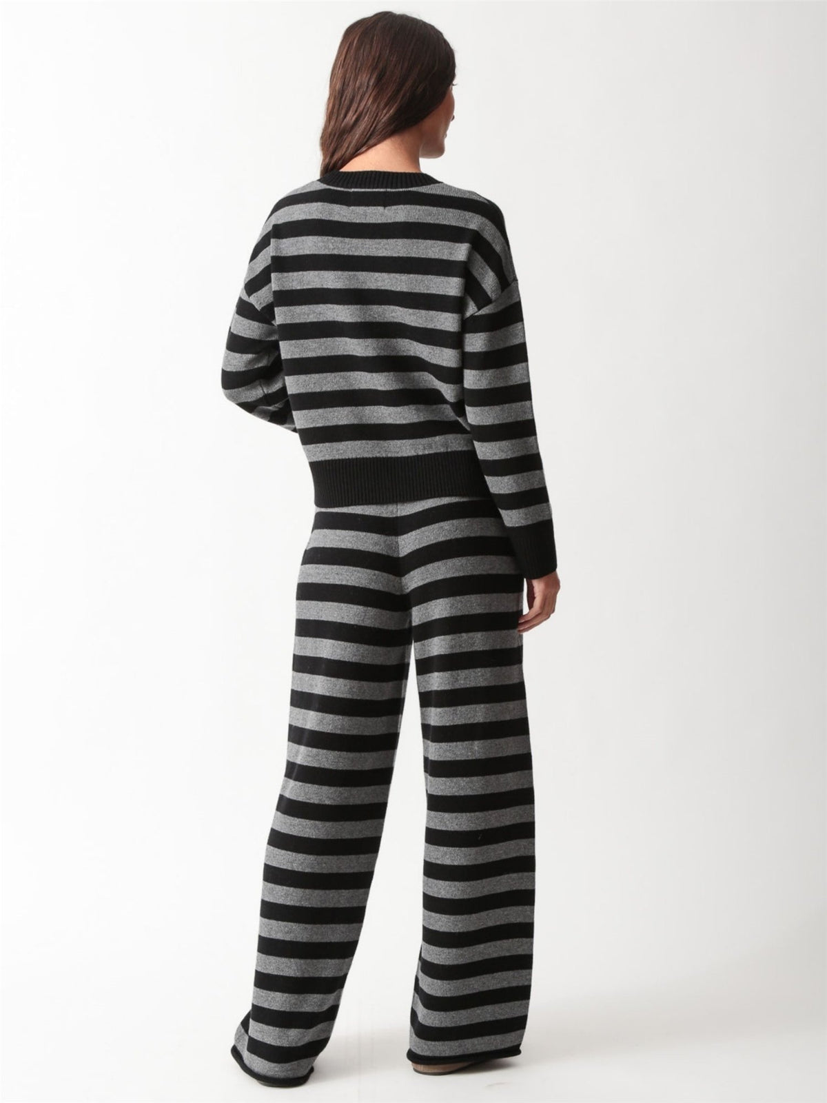 Woman wearing a black and heather grey striped knit crewneck sweater with matching wide-leg drawstring knit pants and white sneakers.