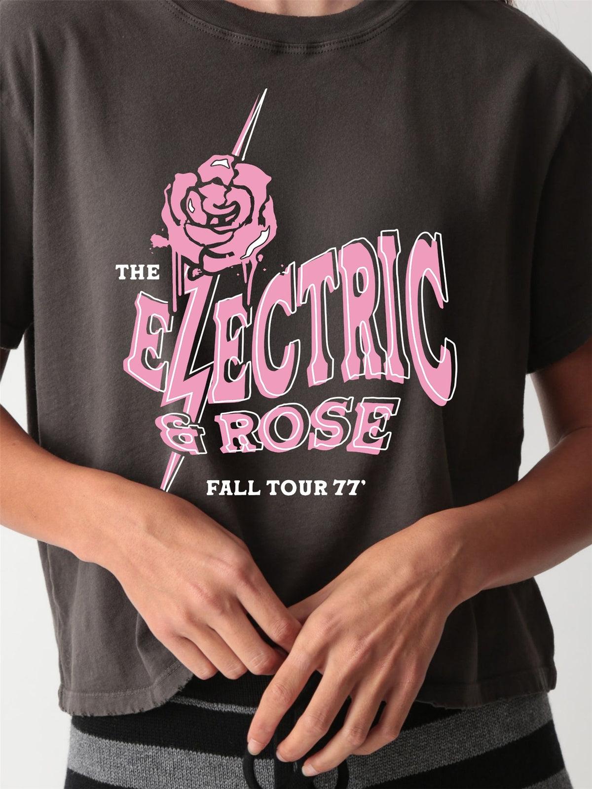 Close-up of a vintage-wash charcoal graphic tee with a pink "The Electric & Rose Fall Tour 77" band-style print featuring a rose and lightning bolt
