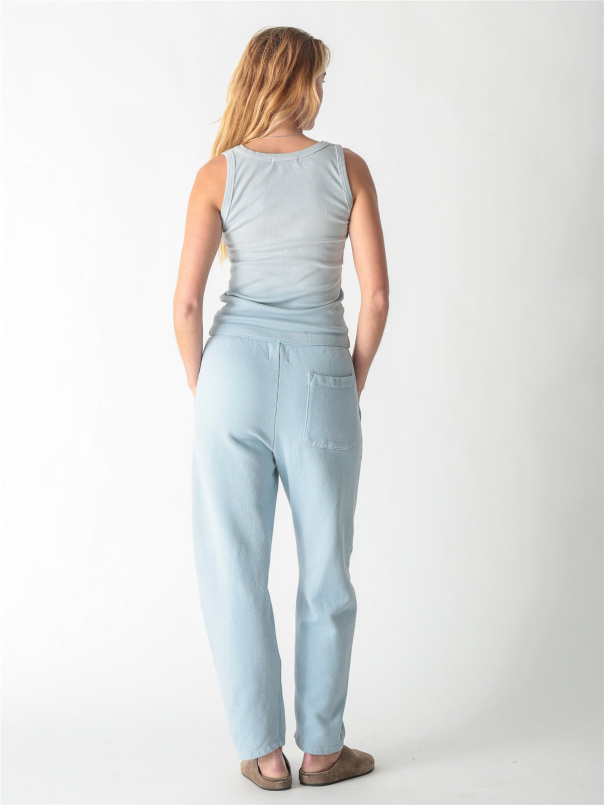 A woman wearing a light blue ribbed scoop neck tank top and matching sweatpants against a white background.