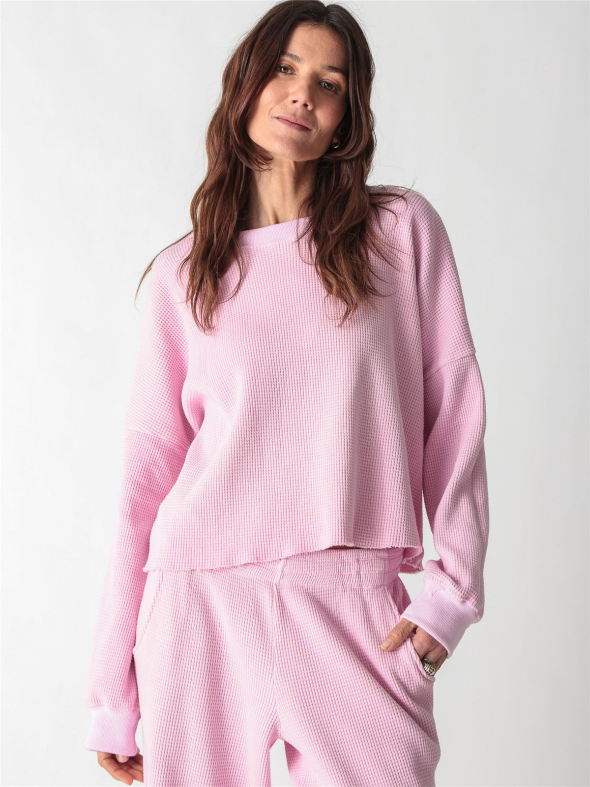 A woman wearing a light pink, long-sleeve waffle-knit lounge set with wide-leg pants against a plain white background.