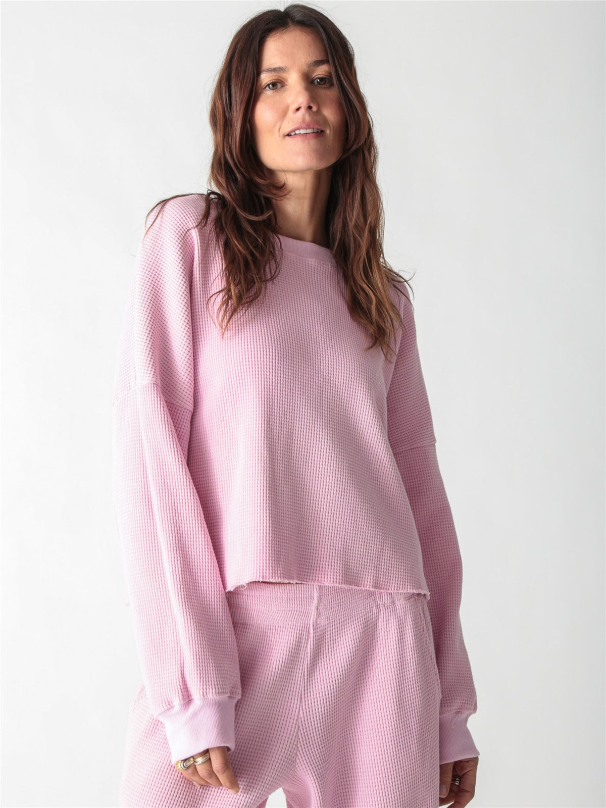 A woman wearing a light pink, long-sleeve waffle-knit lounge set with wide-leg pants against a plain white background.