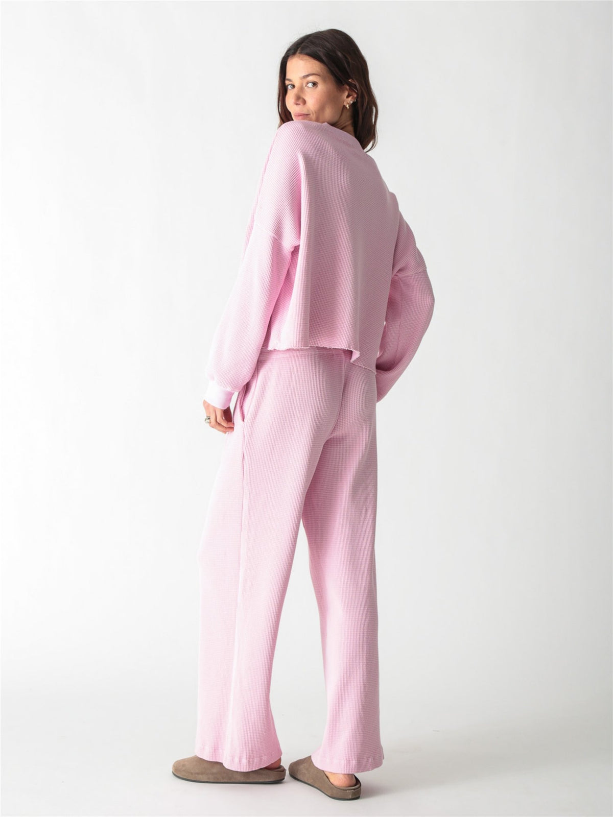 A woman wearing a light pink, long-sleeve waffle-knit lounge set with wide-leg pants against a plain white background.