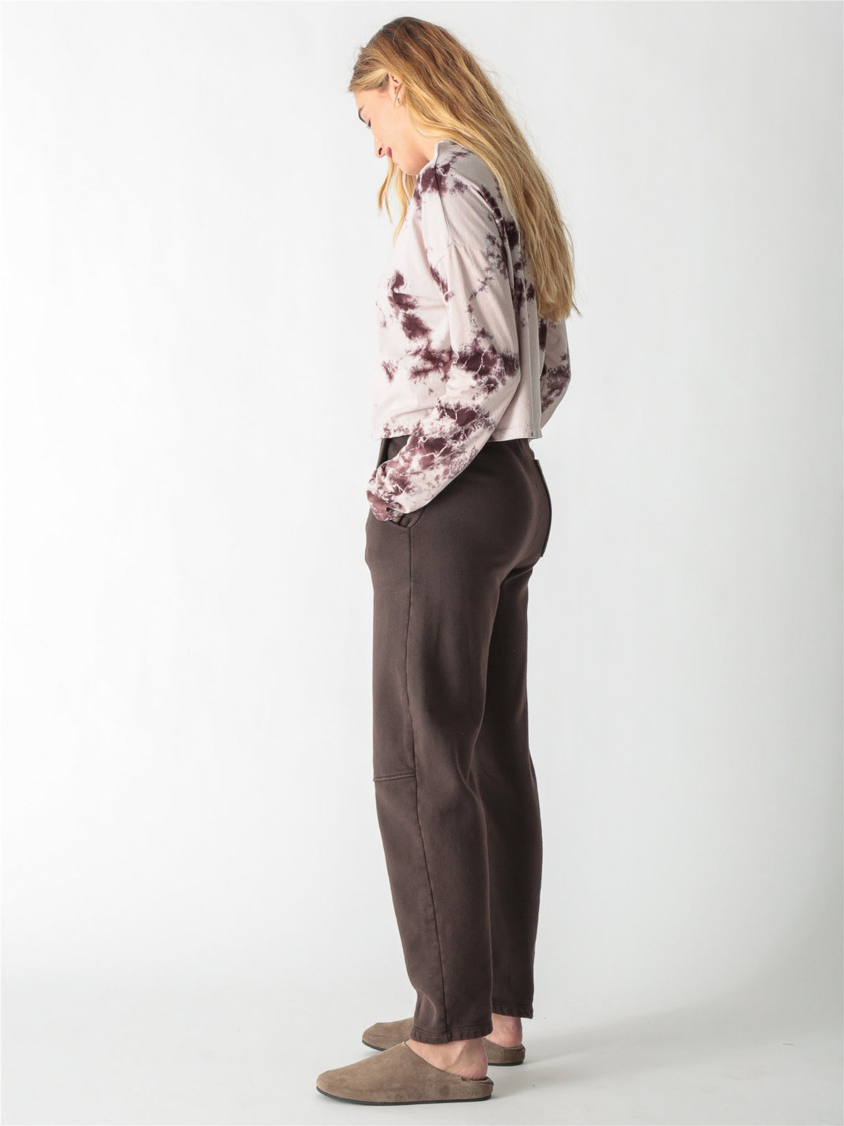 A woman wearing a long-sleeve cropped t-shirt with a cream and brown tie-dye pattern, paired with dark brown pants against a white background.
